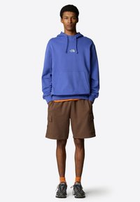 Blue hooded sweatshirt with kangaroo pocket, brown cargo shorts with side pockets, orange socks, and gray outdoor shoes.