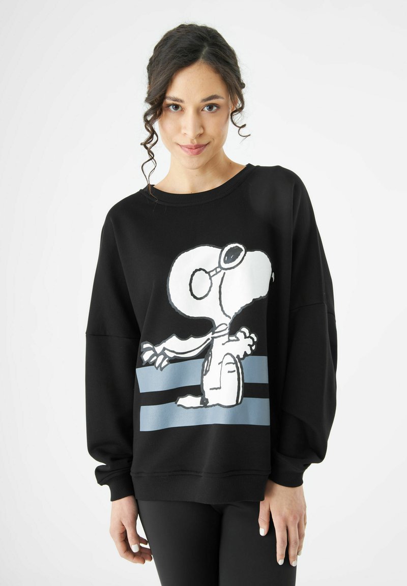 Sweatshirt noir avec un motif Snoopy sur le devant, doté de rayures blanches et bleues. Coupe ample et texture de tissu douce, poignets côtelés.