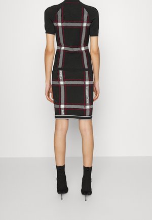 Schwarzes gestricktes Kleid mit kurzen Ärmeln, das ein Schachbrettmuster in Rot und Weiß aufweist und eine taillierte Silhouette hat. Mit weißen Akzenten versehen.