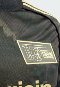 Crna i tamnozelena kamuflažna majica s teksturiranim materijalom, zlatnim detaljima i istaknutim izvezenim logotipom TF Union.