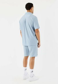 Polo de manga corta de color azul claro con tejido texturizado, combinado con pantalones cortos a juego. Modelo lleva zapatillas blancas y calcetas con detalles negros.