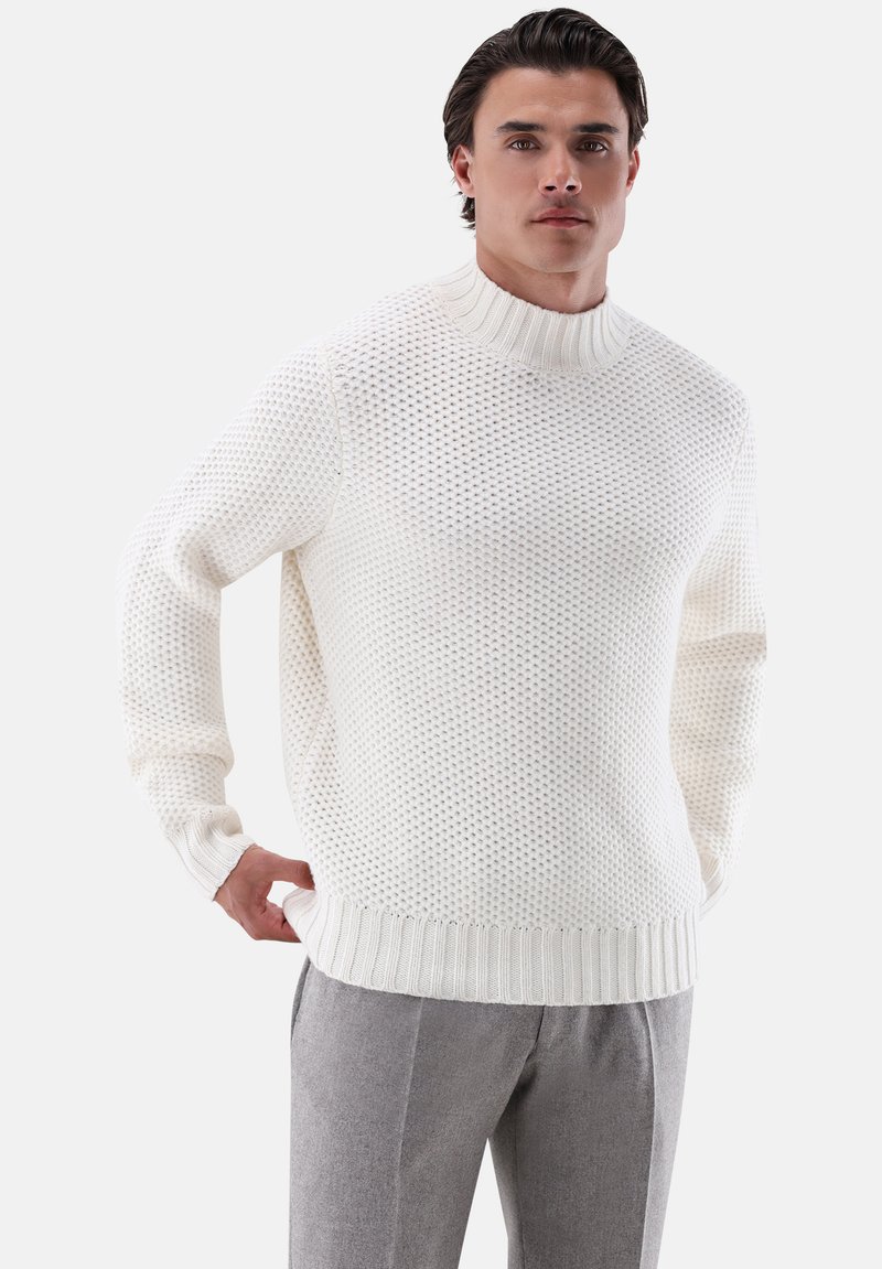 Weißer gestrickter Pullover mit hohem Kragen, der ein strukturiertes Muster sowie gerippte Bündchen und Saum aufweist. Trägt man zu grauen Hosen.