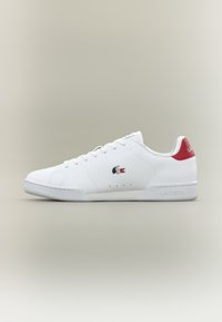 Fehér bőr sneakers, piros sarkú tabbal, fűzős kivitelben, oldalsó perforációkkal és Lacoste logóval az oldalon. Az anyag sima textúrájú.