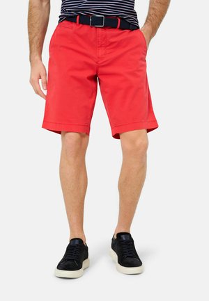Rote Baumwollshorts mit taillierter Passform, mit umgeschlagenem Saum, seitlichen Taschen und einem schwarzen verstellbaren Gürtel. Getragen mit schwarzen Sneakers.