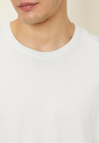 White cotton t-shirt with a crew neckline, smooth texture, and short sleeves, showing the collar area and slight stitching detail.
