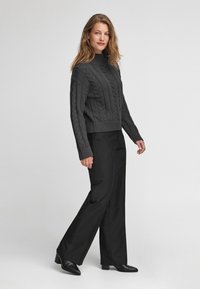 Szary sweter dziany z wzorami warkocza, z wysokim kołnierzem i prążkowanym wykończeniem, połączony z czarnymi szerokimi spodniami i czarnymi botkami na obcasie.