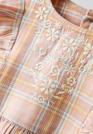 Rózsaszín és sárga kockás ruha fehér virágos hímzéssel. Gyűrt ujjakkal és texturált anyaggal rendelkezik. Figyelemre méltó részletek a felsőrészen.