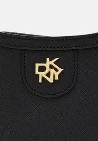 Czarna materiałowa torba z ozdobnym złotym logo DkNY na przodzie. Materiał ma teksturowane wykończenie z widocznymi detalami szwów.