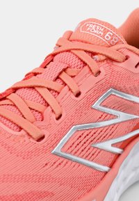 Korallfarbene Mesh-Sportschuhe mit flachen Schnürsenkeln, reflektierendem silbernem Logo und strukturierter Oberfläche. Verfügt über eine gepolsterte Zunge und eine gedämpfte Sohle.