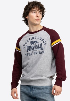 Grau und burgunderfarbenes Sweatshirt mit langen Ärmeln, ausgestattet mit einem Löwengrafik und Text, gelben Akzentstreifen und gerippten Bündchen.