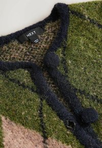 Zaļš un brūns teksturēts kardigans ar tumši ziliem akcentiem, ko rotā apaļš pogu aizdare un uzdruka "NEXT".