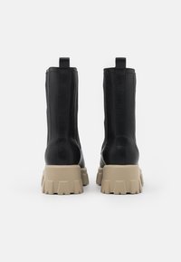 Botas de tobillo de cuero negro con un acabado texturizado, que cuentan con una suela de goma beige gruesa y dos lengüetas para ponerlas y quitarlas fácilmente.