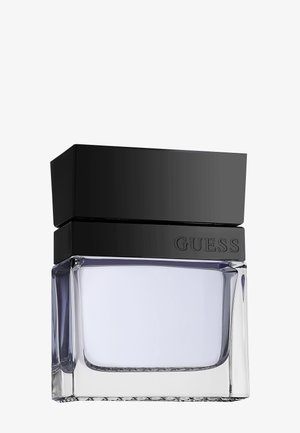 Klar glasparfume flaske med lyse lilla væske, stor sort rektangulær hætte og "GUESS" præget på sort bånd under hætten.