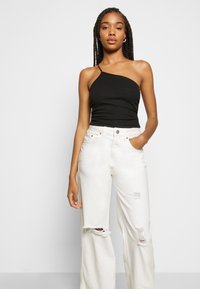 Top preto de um ombro só, em malha canelada, combinado com jeans brancos de perna larga destruídos, com rasgos e bordas desfiadas. Design simples e moderno.