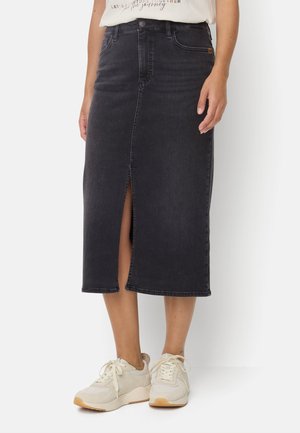 Schwarzer Denim-Midirock mit Frontschlitz, getragen mit weißen Sneakers und einem weißen, in den Rock gesteckten T-Shirt.