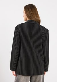 Black pinstriped blazer featuring a structured design, wide lapels, and long sleeves. Material appears smooth with a slightly textured finish.
