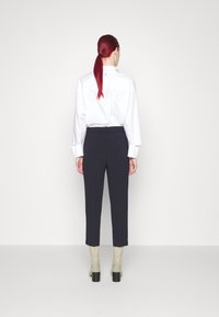 Camisa blanca de manga larga y pantalones oscuros. La camisa tiene un diseño entallado; los pantalones son ajustados con una textura suave. Botas con tacón grueso.