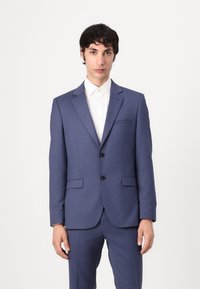 Traje azul marino con un corte ajustado, que presenta dos botones, solapas con muesca y bolsillos laterales, combinado con una camisa blanca con cuello.