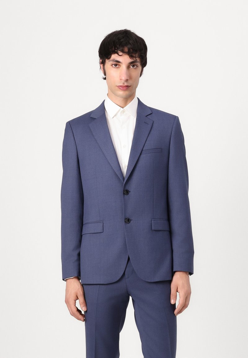 Traje azul marino con un corte ajustado, que presenta dos botones, solapas con muesca y bolsillos laterales, combinado con una camisa blanca con cuello.