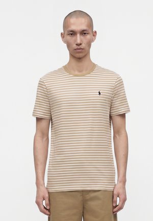 Mand iført beige og hvidstribet kortærmet skjorte med lille sort logo på venstre bryst og beige bukser, stående mod en hvid baggrund.