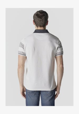 Mand iført hvid kortærmet polotrøje med grå accenter og mørk krave, kombineret med blå jeans, vist bagfra.