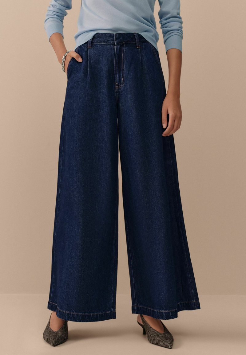 Wijde jeans in donkere denim met een hoge taille, voorzien van zijzakken en contrasterende stiksels. Gekocht in combinatie met textuur hakken.