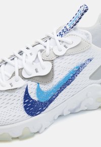 Zapatillas Nike con una parte superior de malla blanca con acentos en azul y azul oscuro, superposiciones grises y una suela de goma texturizada.