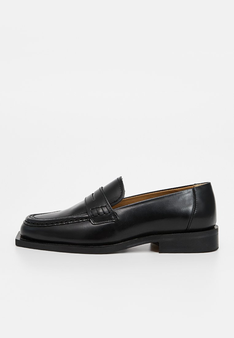 Mocassino in pelle nera con un design classico, dotato di punta a mocassino, cuciture decorative e tacco basso impilato. Tessuto liscio e finitura lucida.