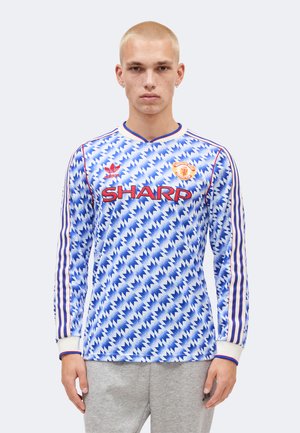 Ung mand med kort blondt hår iført en blå og hvid mønstret Manchester United fodboldtrøje med lange ærmer og "SHARP" sponsorlogo.
