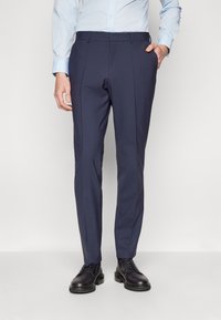 Sötétkék, szabott nadrág sima fel�ülettel, slim fit szabással, két oldalsó zsebel és elöl gyűrődéssel, fekete elegáns cipővel párosítva.