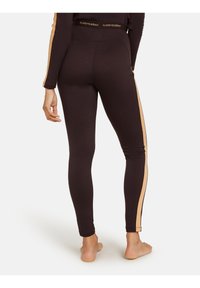 Bruine legging met een hoge tailleband, voorzien van zijpanelen in een lichtere tan kleur en een logoband rond de taille. Glad textuur.