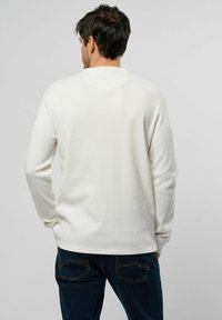 Witte langekoe tweede shirt met een geribbelde textuur en ronde hals, gecombineerd met donkerblauwe broek met twee achterzakken en zichtbare stiksels.