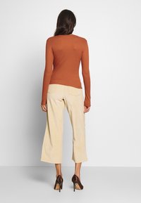 Ribbad, långärmad topp i rostfärgad nyans ihop med vida beige kordbyxor, som har bakfickor och bruna klackskor.
