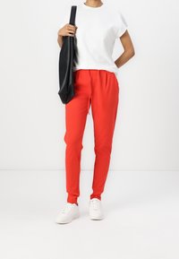 Röda tapered sweatpants med elastisk midja, sidofickor och snörningsdetalj, i kombination med en vit t-shirt och vita sneakers.