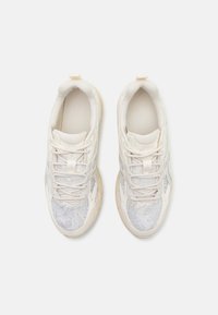 Beežid tossud tekstuurse võrguga pealiskihil, kontrastse kreemika tallaga ja paeltega. Kangal on peen muster ning kannal on silt.