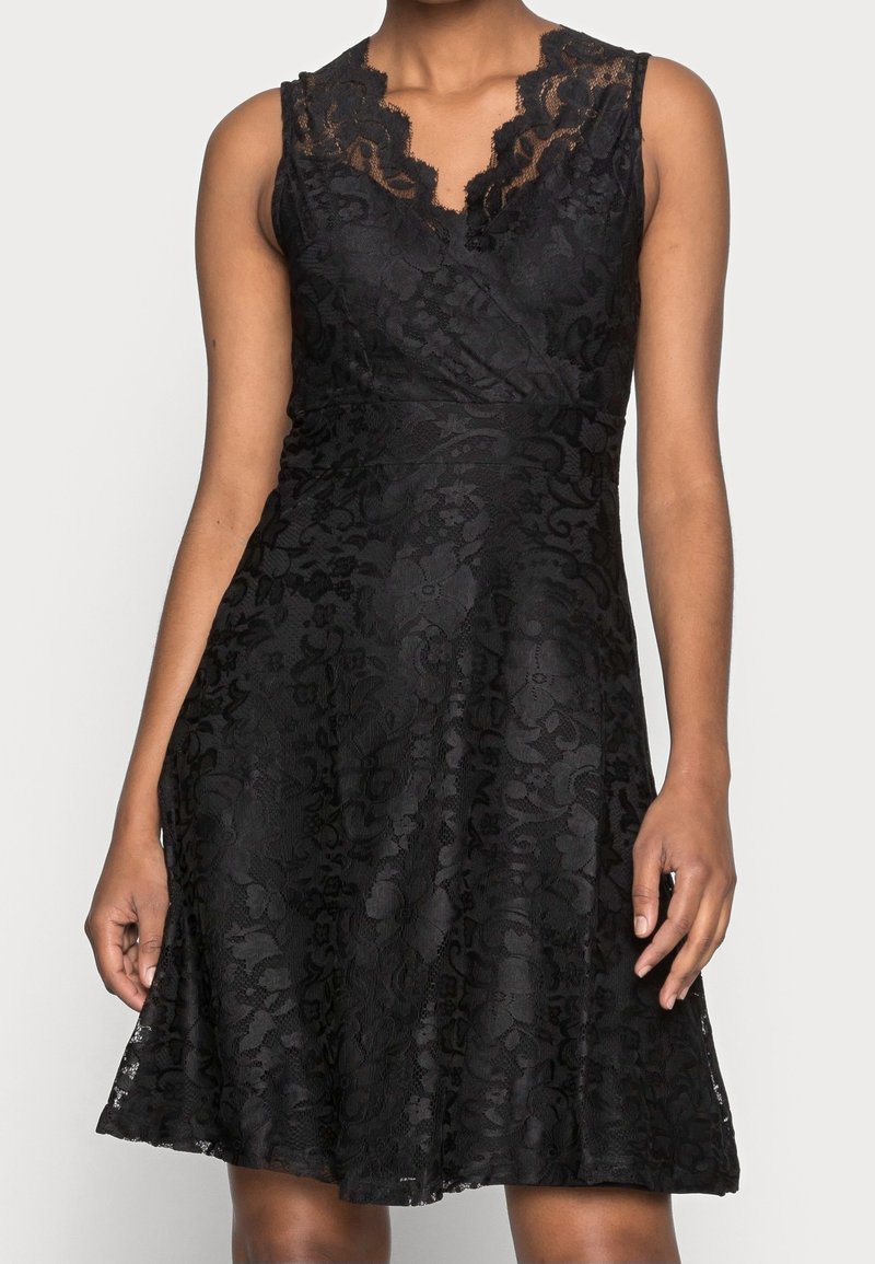 Robe noire en dentelle sans manches avec motif floral, encolure en V avec bordure en dentelle festonnée et taille ajustée s'évasant en jupe trapèze.