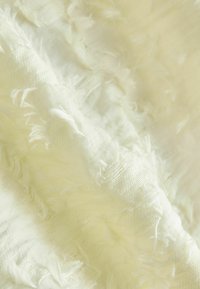 Tissu texturé de couleur jaune pâle avec des bords effilochés, présentant un matériau doux et léger ainsi qu'une surface ondulée et sinueuse.