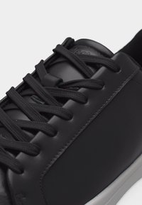 Κοντινό πλάνο μαύρου δερμάτινου αθλητικού παπουτσιού με μαύρα κορδόνια και λευκή σόλα, που αναδεικνύει την ομαλή υφή και τις λεπτομέρειες των ραφών.