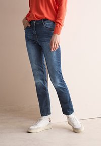Blå denimjeans med rak benstil, som har en framficka, subtil blekning och är kombinerade med vita sneakers och en röd tröja.