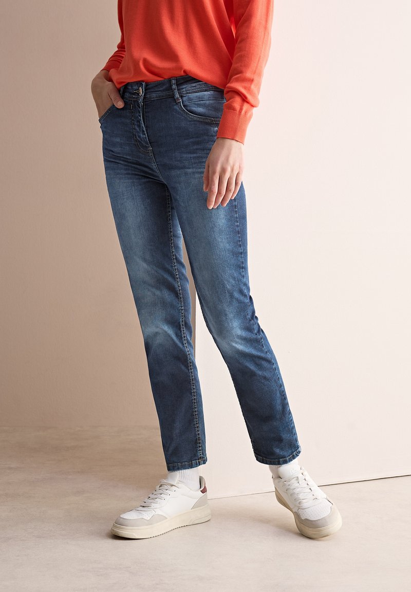 Blå denimjeans med rak benstil, som har en framficka, subtil blekning och är kombinerade med vita sneakers och en röd tröja.