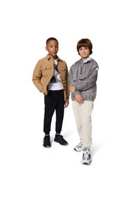 Two boys stand side by side. One wears a tan padded jacket and black pants; the other has a patterned grey pullover and cream trousers.