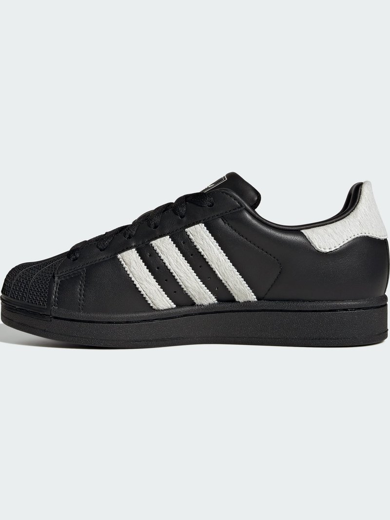 Czarny skórzany sneaker z białymi, teksturowanymi trzema paskami, zaokrąglonym noskiem i czarną podeszwą. Posiada sznurowanie z przodu oraz charakterystyczny wzór na czubku buta.