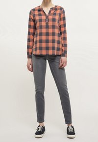 Rutigt långärmad skjorta i orange och marinblått, med v-ringning och knappslå. Kombinerad med grå slim-fit jeans och svarta sneakers.