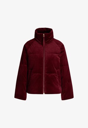 Veste matelassée bordeaux en tissu doux, avec un col haut, fermeture éclair et poches latérales, présentant une texture matelassée et des manches raglan.