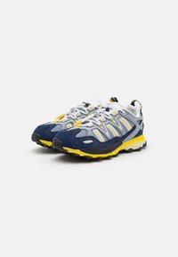 Sportskor med en marinblå och gul design, med en överdel av mesh, förstärkt tå och en texturerad svart gummisula.
