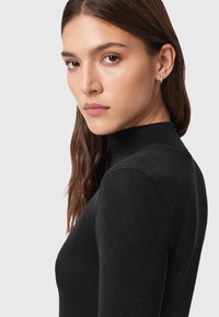 Maglione a collo alto nero a coste con maniche lunghe, caratterizzato da una silhouette aderente e un collo alto. Texture liscia e design minimal.