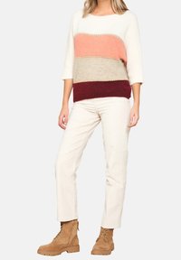 Neulepaita vaakaraidoilla värissä kerma, vaaleanpunainen, beige ja viininpunainen; kolme neljäsosahihat; yhdistetty kermaan vivahtaviin housuihin ja vaaleanruskeisiin nauhallisiin saappaisiin.