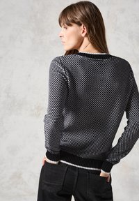 Pull en tricot noir et blanc avec un motif géométrique texturé, col, poignets et ourlet côtelés, de coupe ajustée.