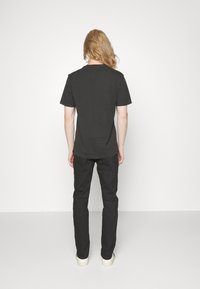 T-shirt nera in cotone con maniche corte, scollatura rotonda e vestibilità rilassata, abbinata a pantaloni neri e sneakers bianche, vista da dietro.