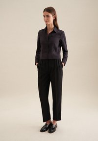 Camicetta nera cropped con bottoni e colletto, abbinata a pantaloni neri a vita alta plissettati e mocassini neri. Tessuto dalla consistenza liscia.